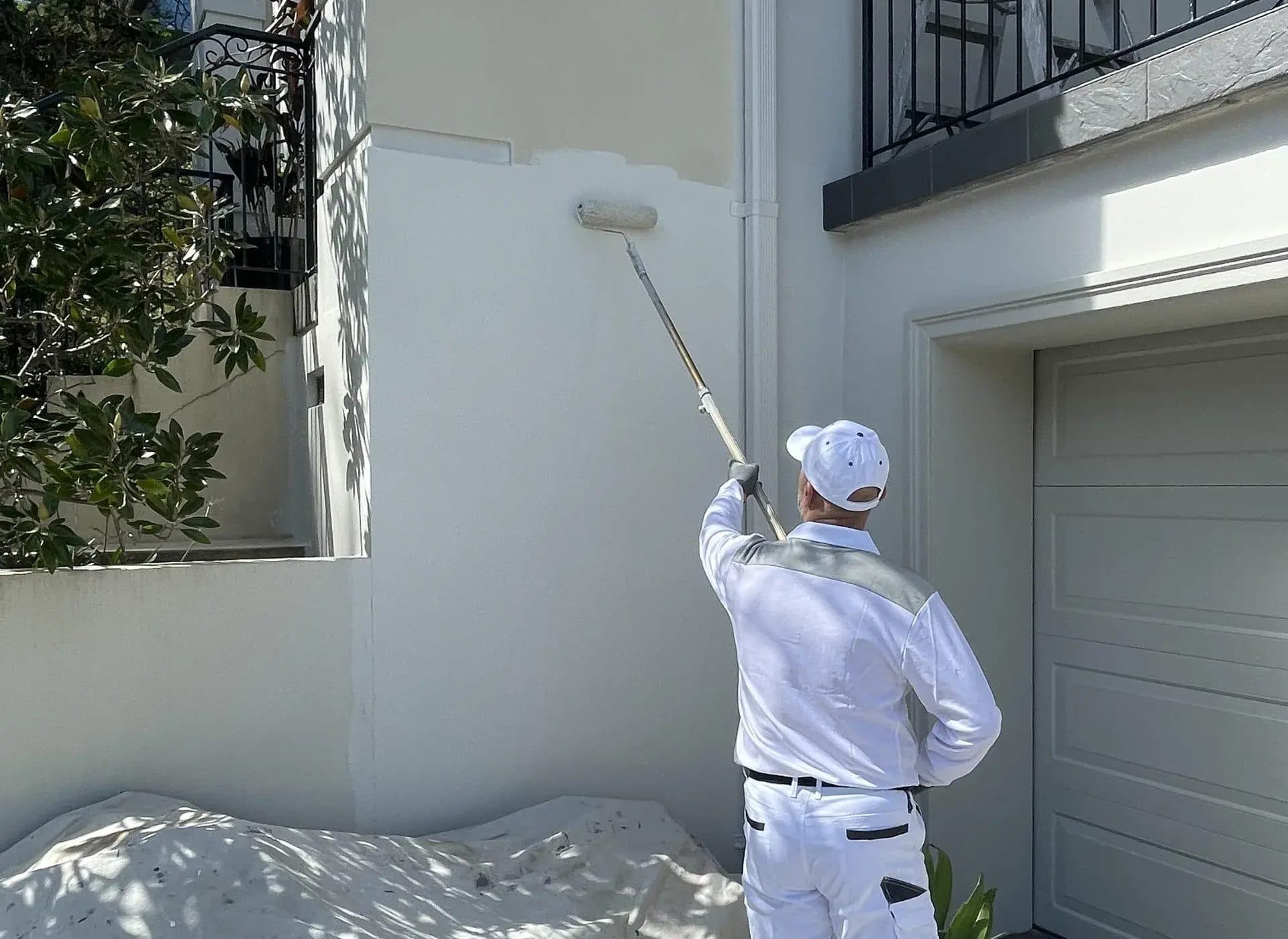 Painter using an extension pole roller to repaint a rendered house exterior
