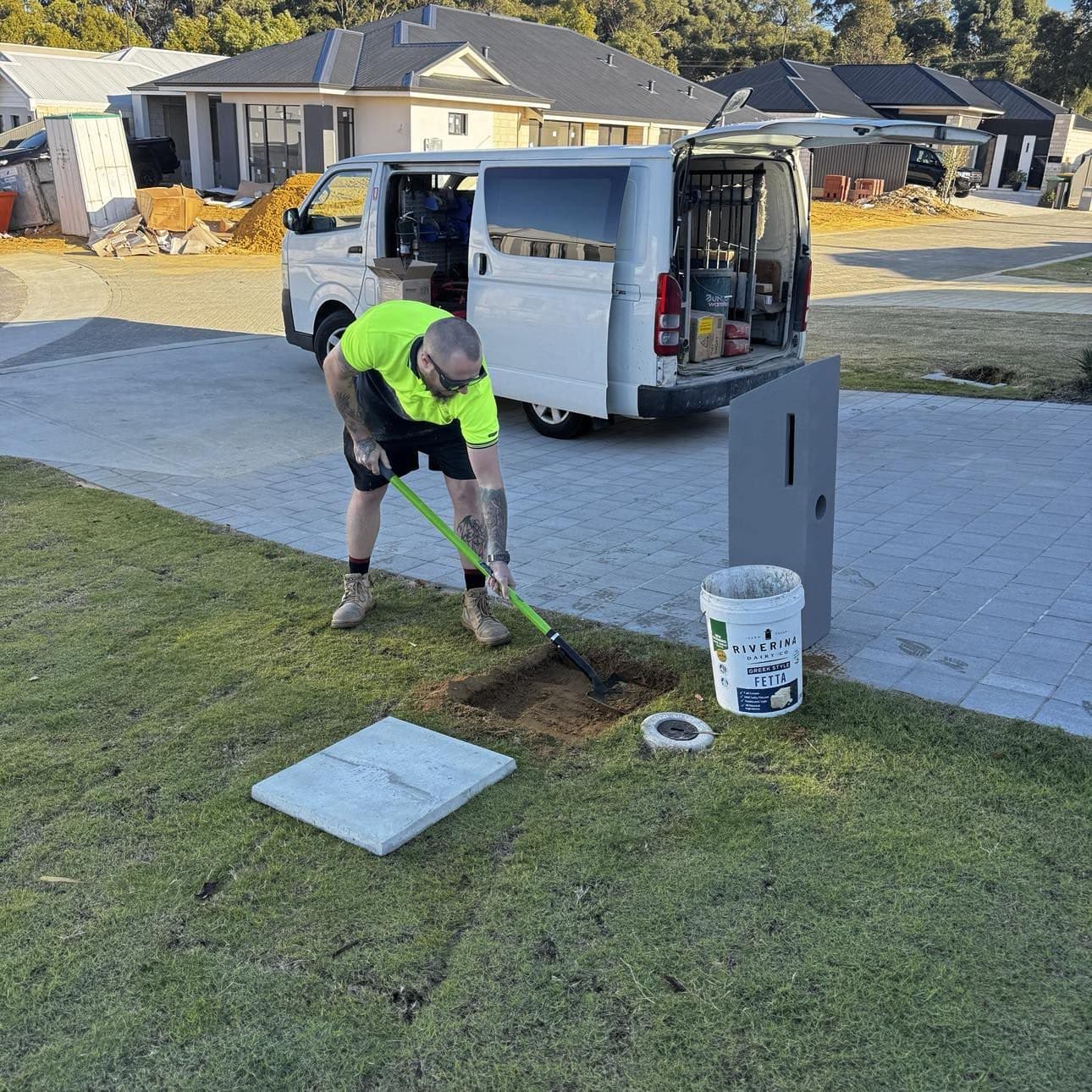 Tradie digging a footing hole on a new-estate lawn to install a pillar letterbox