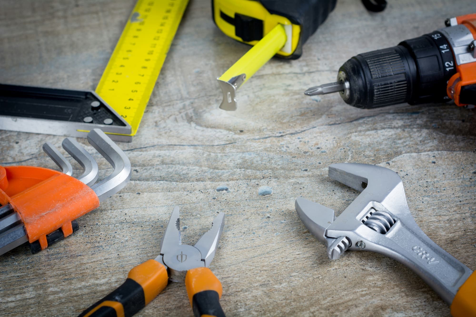 Assorted hand tools — tape measure, drill, pliers, wrench and hex keys — laid out on a timber surface
